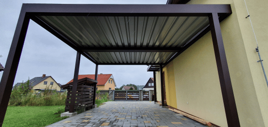 Hliníkový prístrešok s tmavým rámom nad dlaždenou plochou pri dome